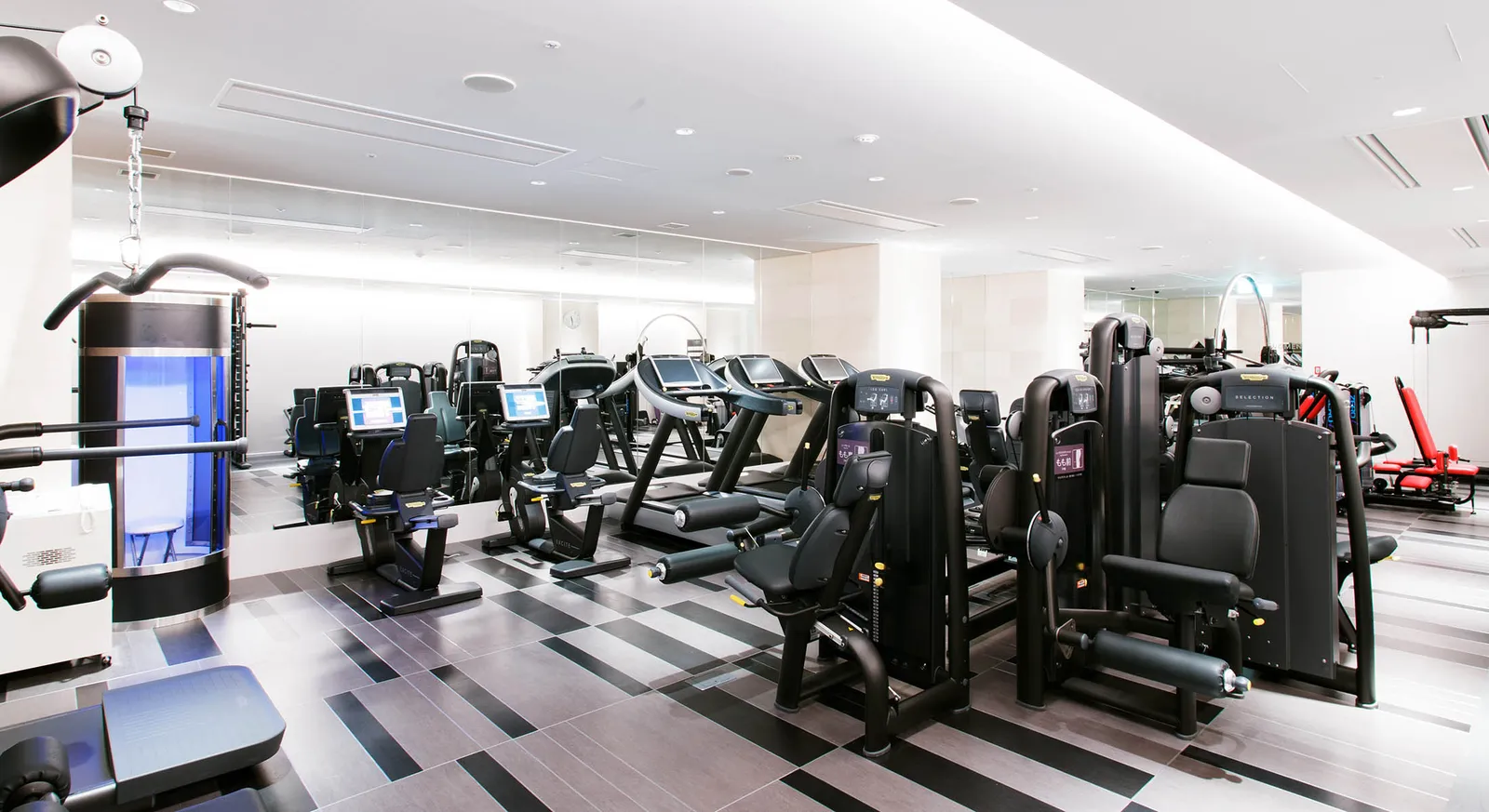 The Jexer Tokyo gym: weight machines and cardio equipment in a white room.