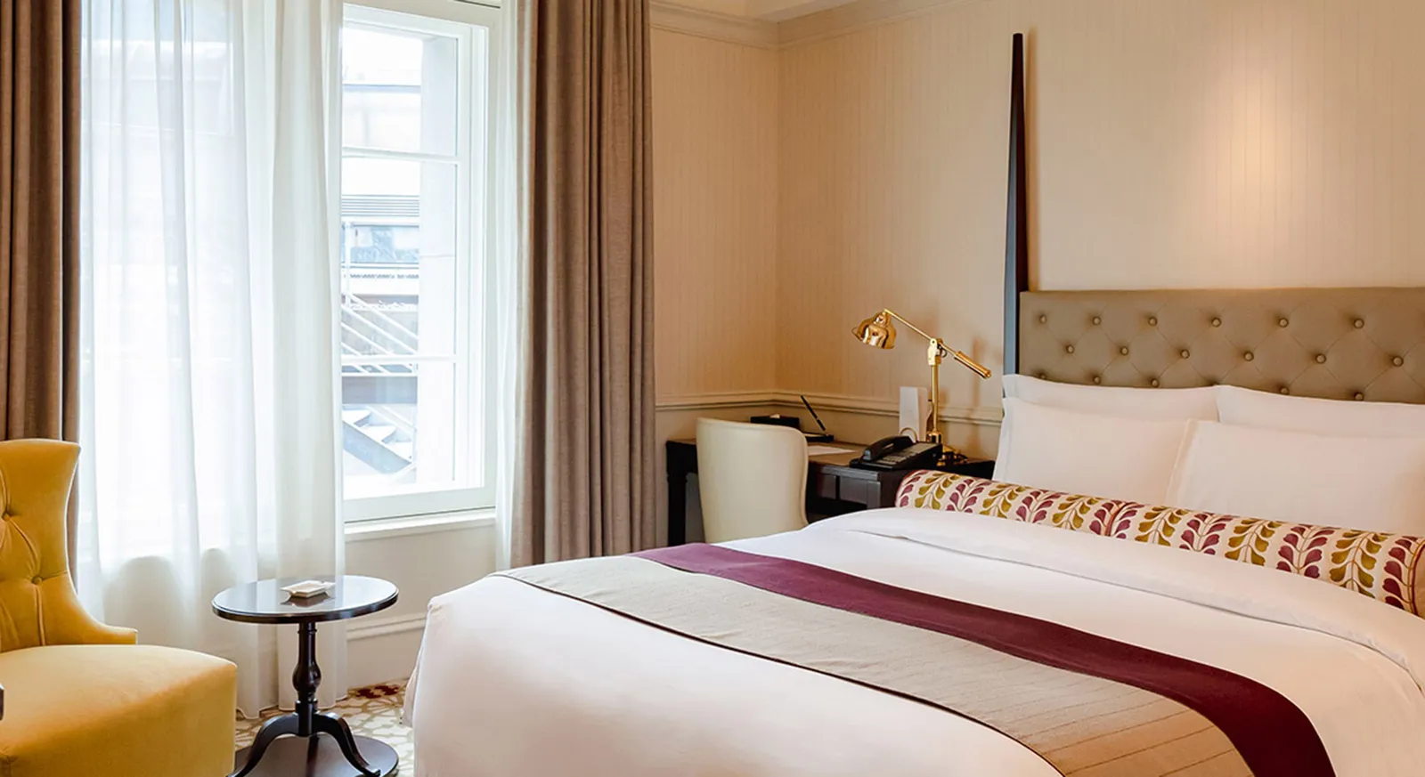 A Classic room with the bed and its plum-patterned bolster, a yellow armchair, the desk and the curtained window.