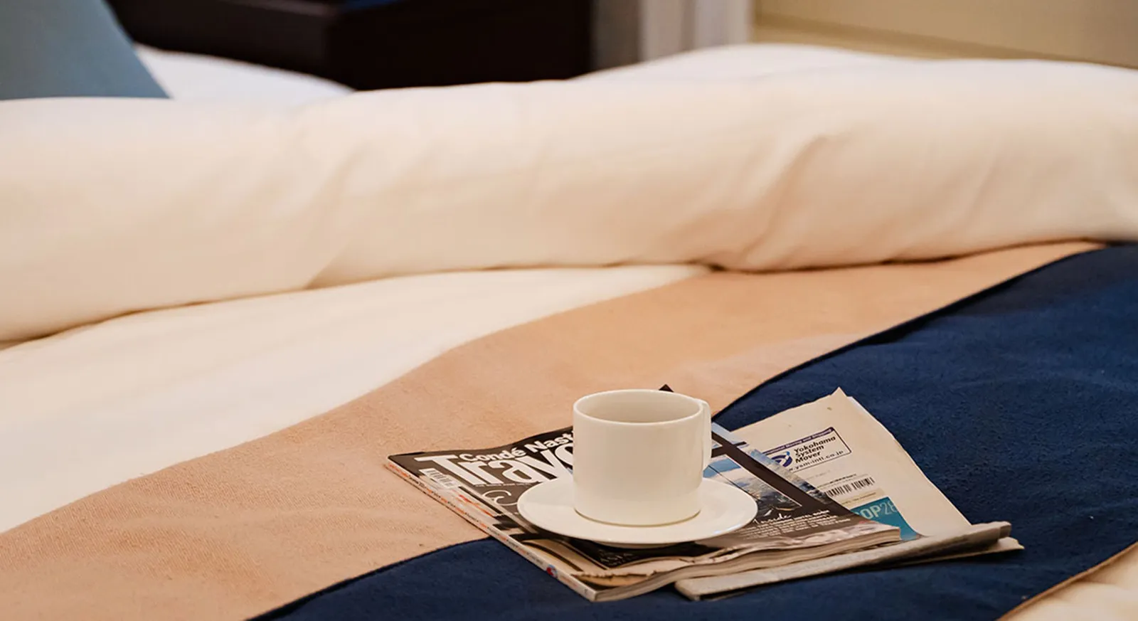 A detail of a Dome Side bed: the blue throw, a newspaper and a cup of coffee.
