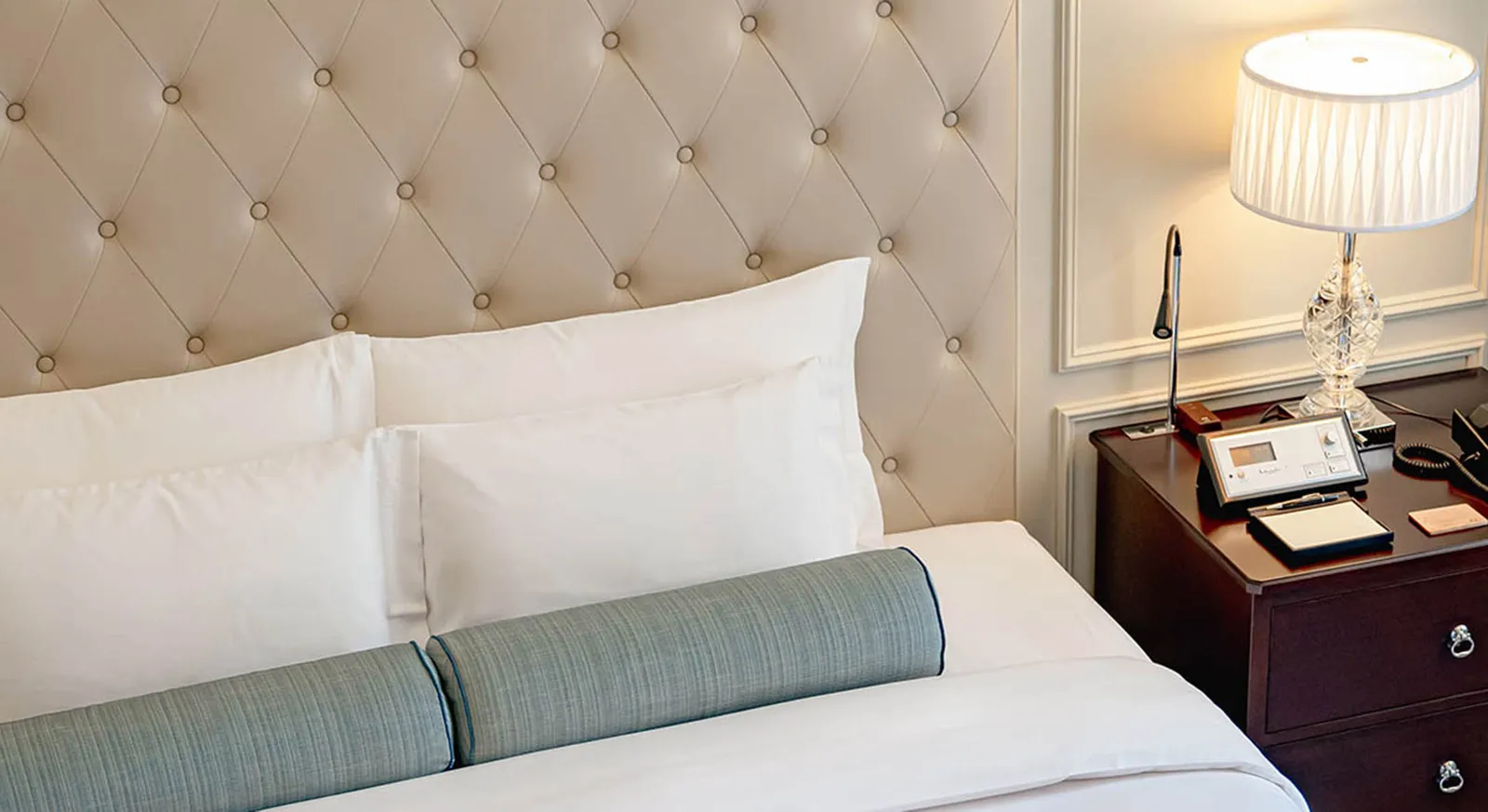 A Junior Suite bed with its buttoned headboard, pale blue bolsters and the crystal lamp on the bedside table.