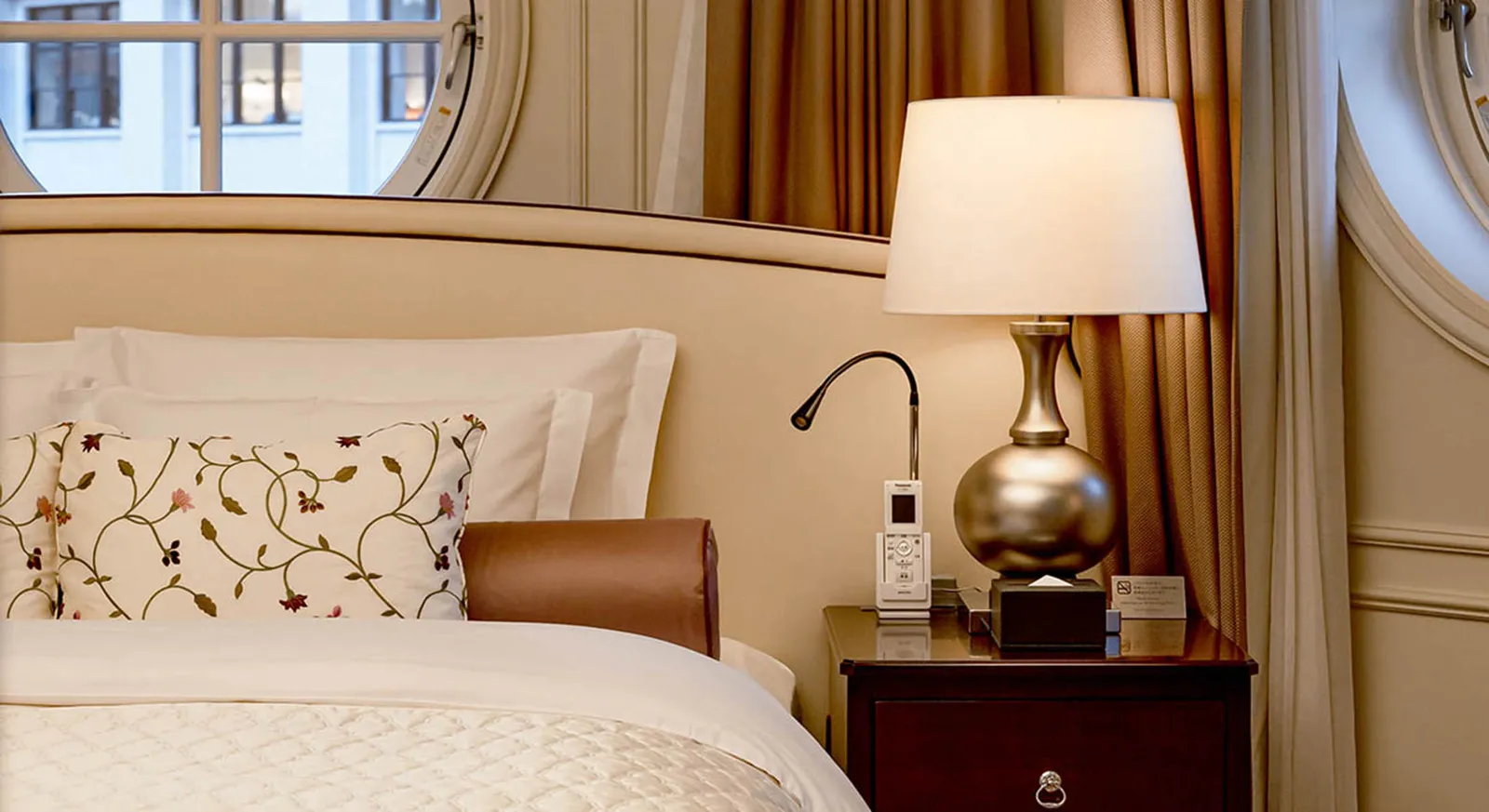 A Maisonette Suite bedroom, with the round window above the headboard, the embroidered cushions and the silver lamp.