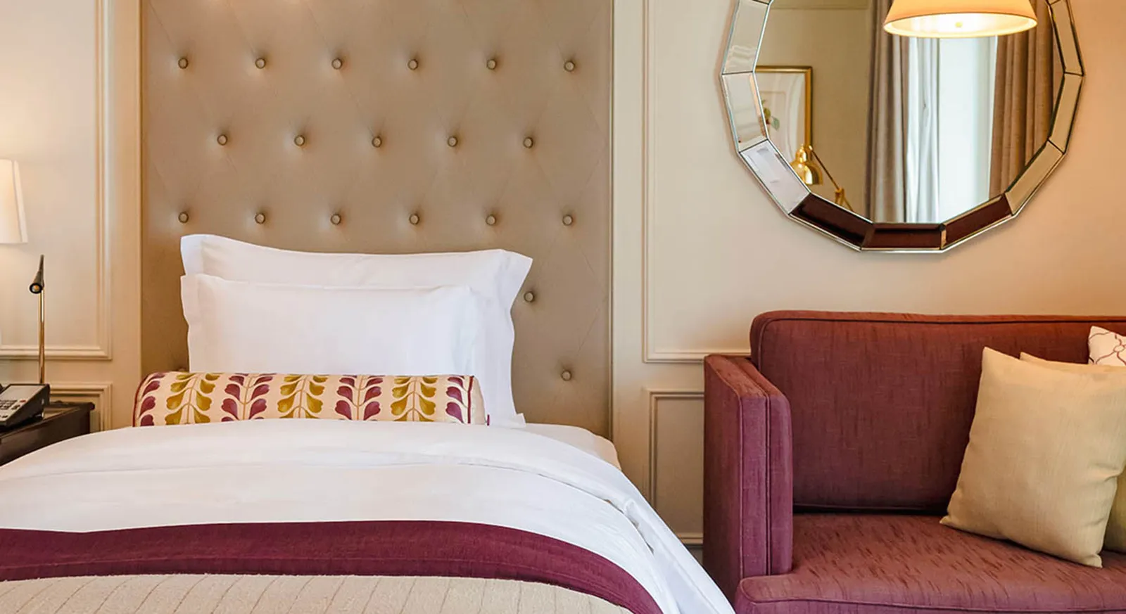 A South Wing room: the bed with its buttoned headboard, the plum sofa and the faceted mirror.
