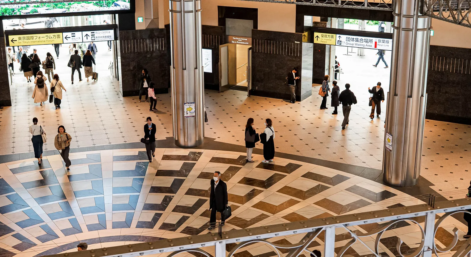 The Marunouchi South Exit concourse seen from the balustrade: the patterned floor, the signs for Tokyo International Forum and the travellers.