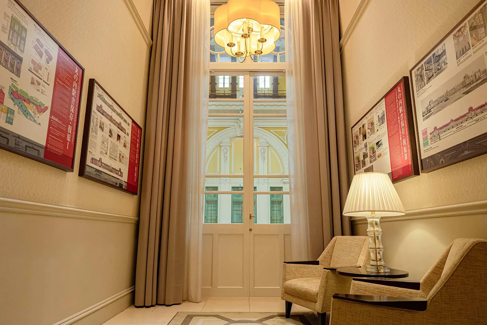 The Archive Balcony: a corridor with armchairs and archive drawings on the walls, and a glass door onto the station’s yellow dome.