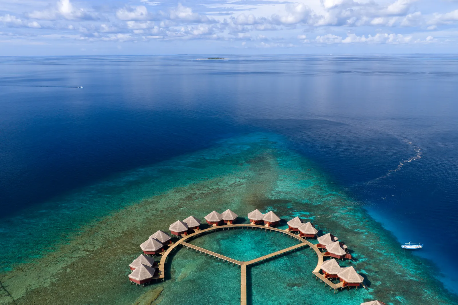The water villas set in an arc on the edge of the reef, joined by walkways, where the pale lagoon drops into deep blue.