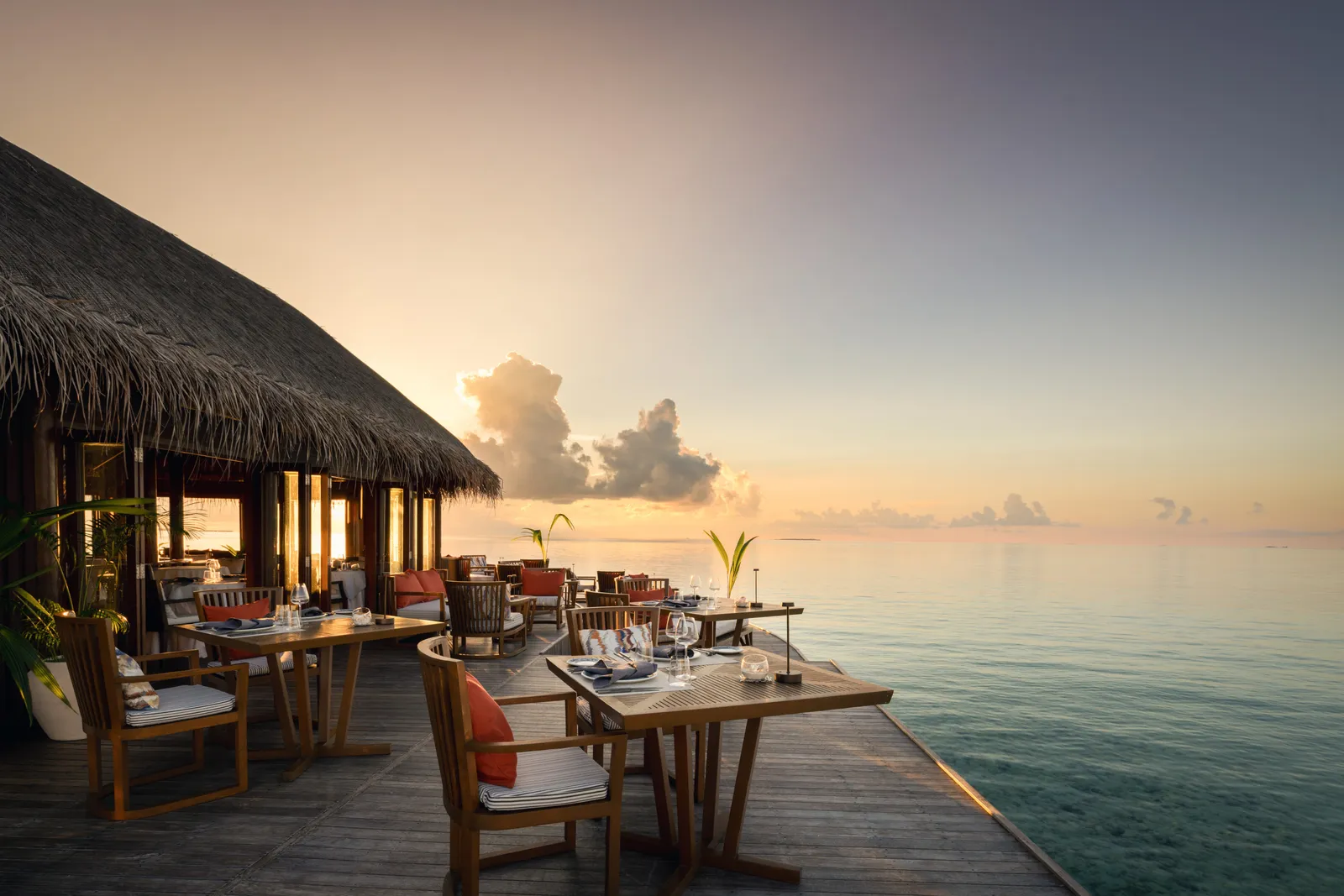 Muraka’s deck over the water at sunset, tables laid under the thatched roof and a calm sea.