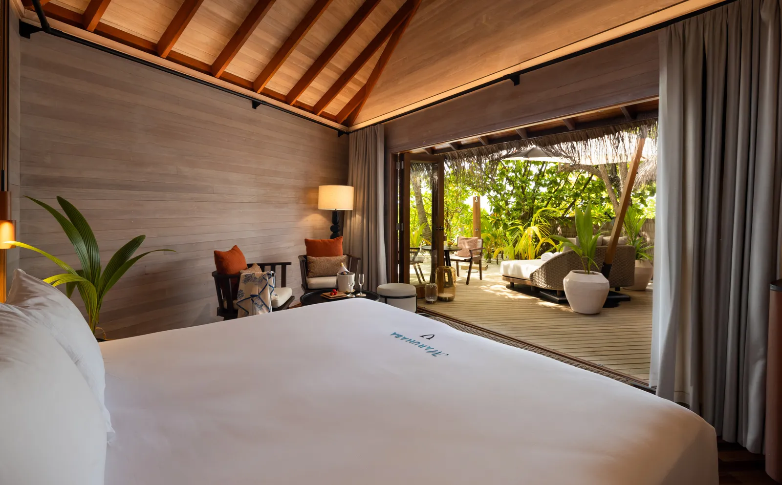 A Beach Villa: the white bed, the timber ceiling and the glass doors open onto the deck in the tropical garden.