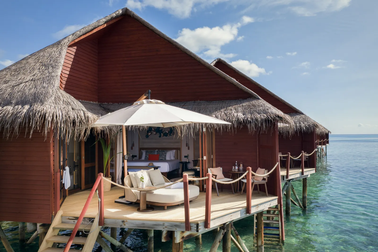 An Overwater Villa on stilts, with its deck, parasol, sofa and the steps down into the lagoon.