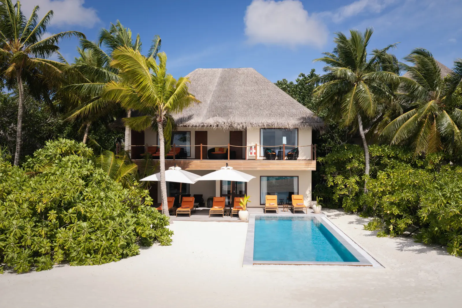 The 2-storey Three Bedroom Beach Residence among the palms, its private pool on the sand and loungers in front.