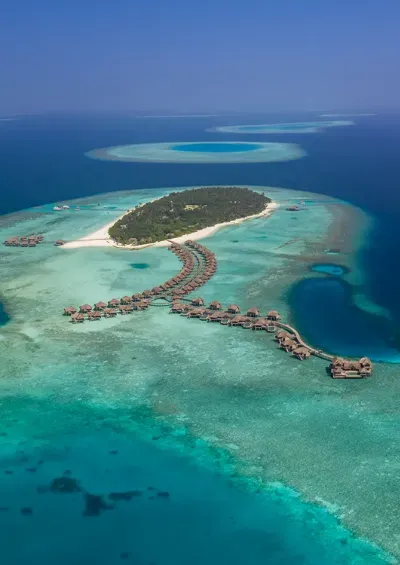 The island from the air, its water-villa jetties curving into the lagoon and the reef around it.