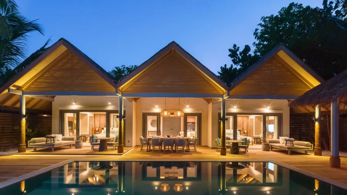 The main house of the Four Bedroom Beach Pool Residence at night, its lights in the pool.