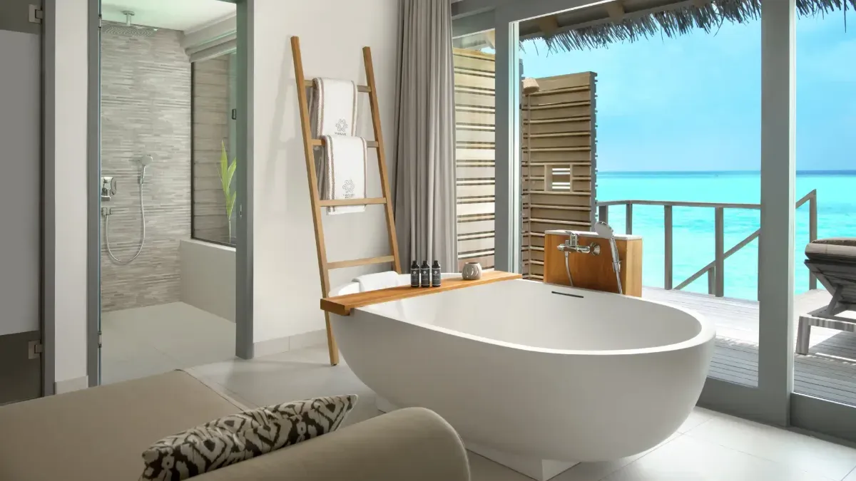 The freestanding bath of an Overwater Deluxe Pool Villa, facing the glass wall onto the lagoon.