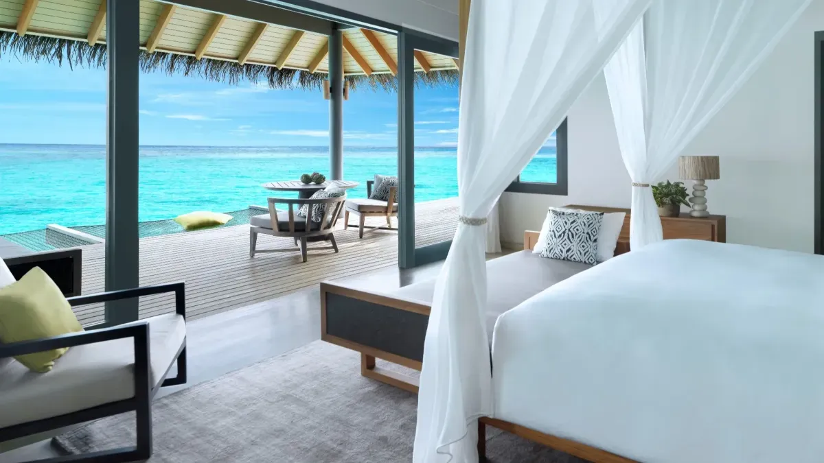 An Overwater Villa bedroom, its canopy bed open to the deck and the lagoon.