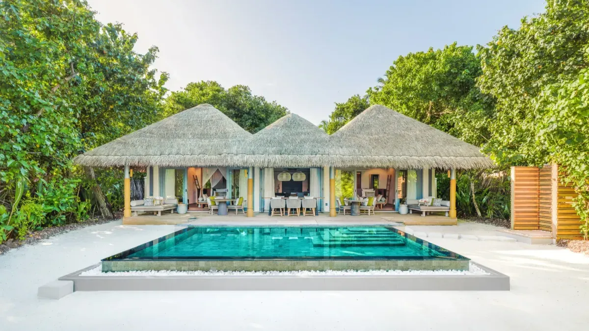 A Two Bedroom Beach Pool Residence from the front, its pool before it, among the trees.