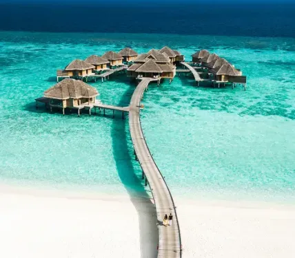 The wooden jetty from the beach to the water villas, with 2 people walking along it.