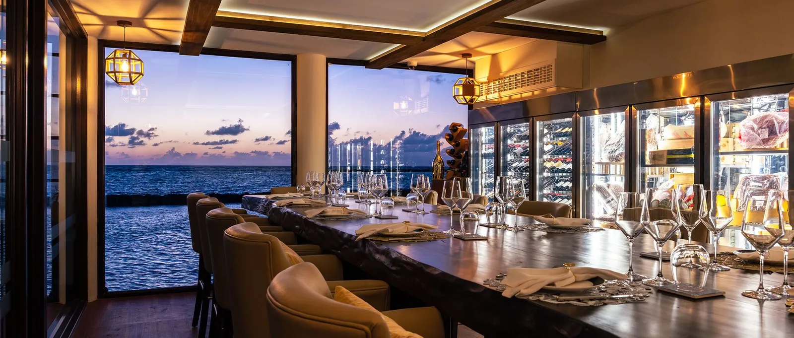 Cellar at NÜ’s long table at dusk, between the wine cabinets and the windows open onto the lagoon.