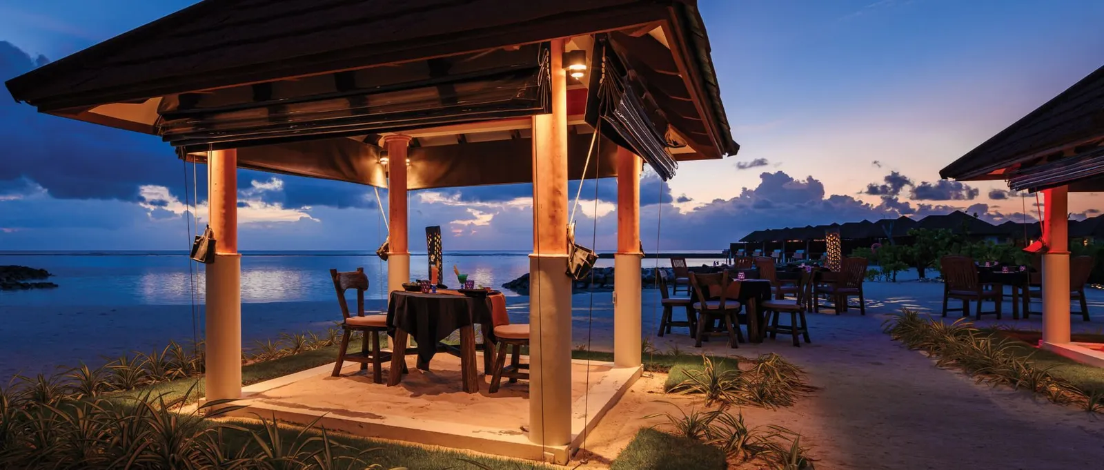 Charcoal’s lit gazebo on the sand at dusk, with tables laid for dinner.