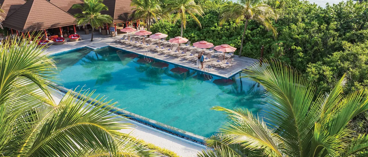 Bay Rouge’s infinity pool among the palms, with sun loungers and red parasols along its edge.