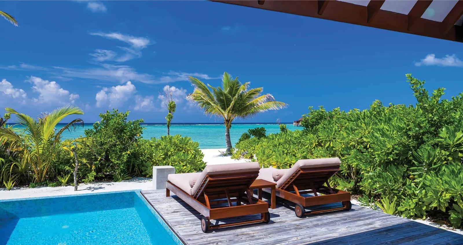 2 timber loungers beside a Beach Villa with Pool’s plunge pool, with palms and the sea behind.
