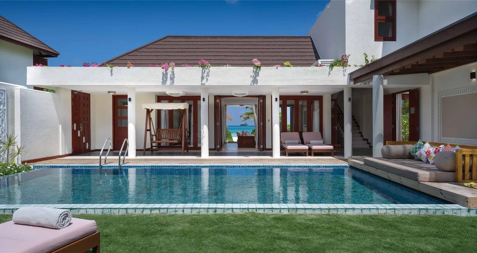 The Majlis Residence courtyard: the long pool, the lawn and the white 2-storey house with its doors open.