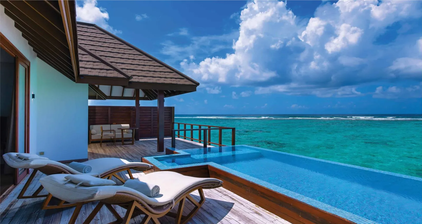 The Water Suite’s terrace with its infinity pool, the loungers and the lagoon under a cloudy sky.