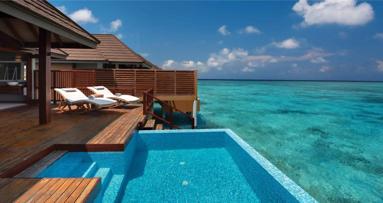 A Water Villa with Pool’s deck pool facing the open sea, with white loungers.