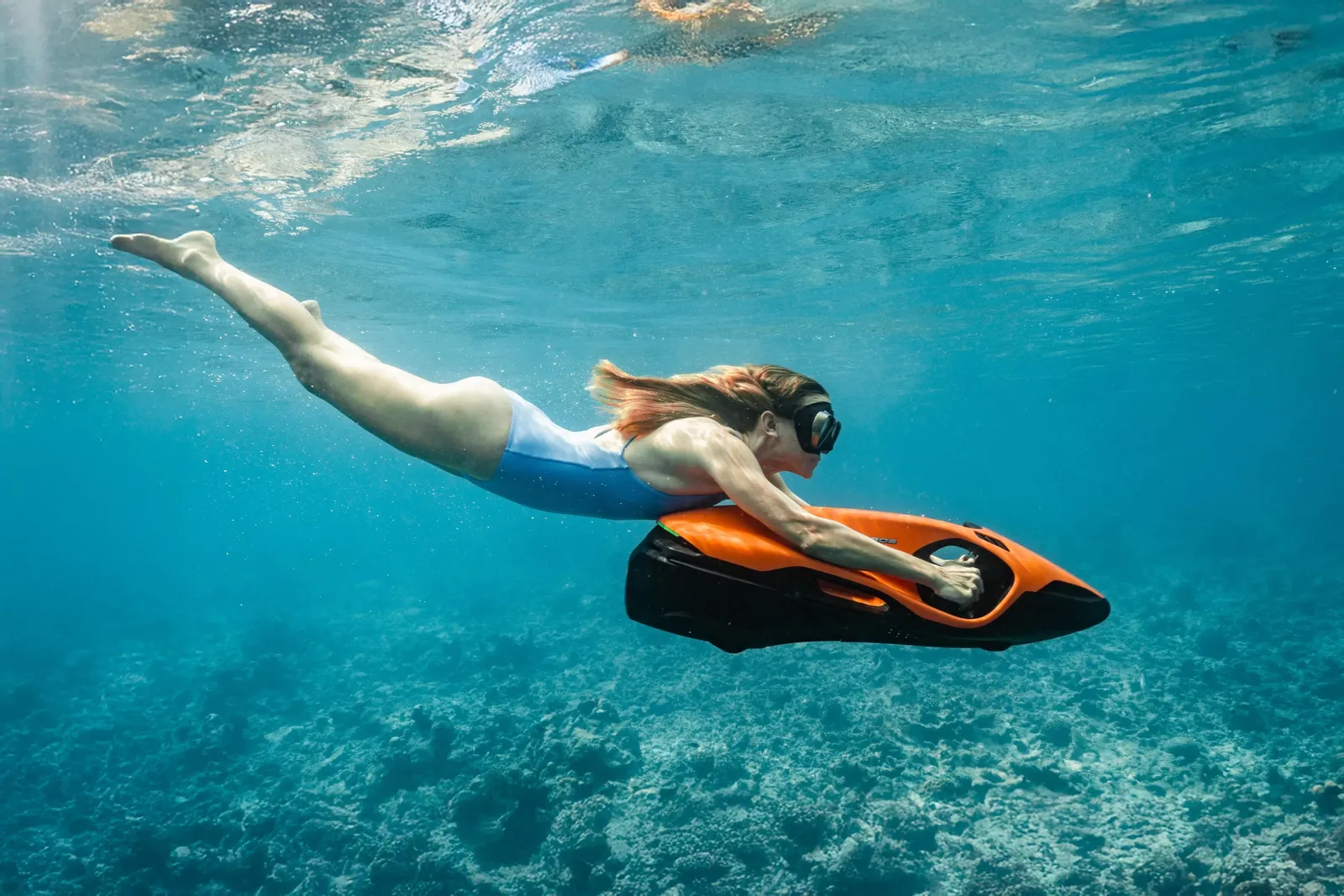 A swimmer with an underwater scooter over the pale seabed