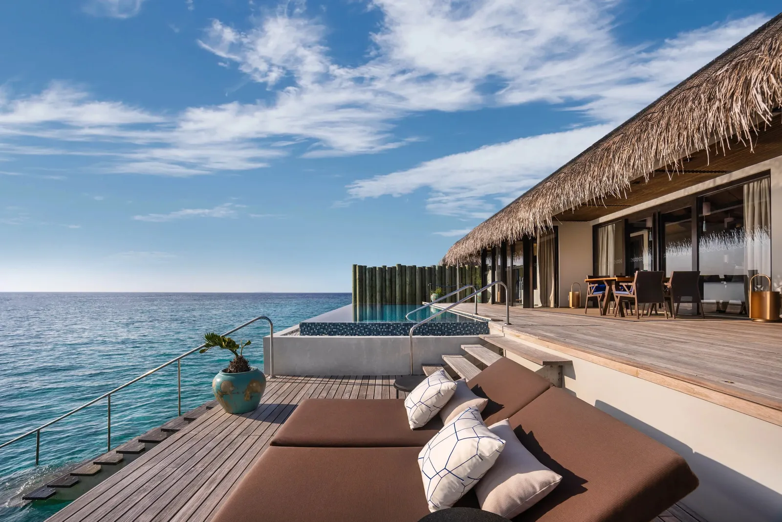The deck of a Sunset Deluxe Water Pool Villa: cushions, the pool and the open sea
