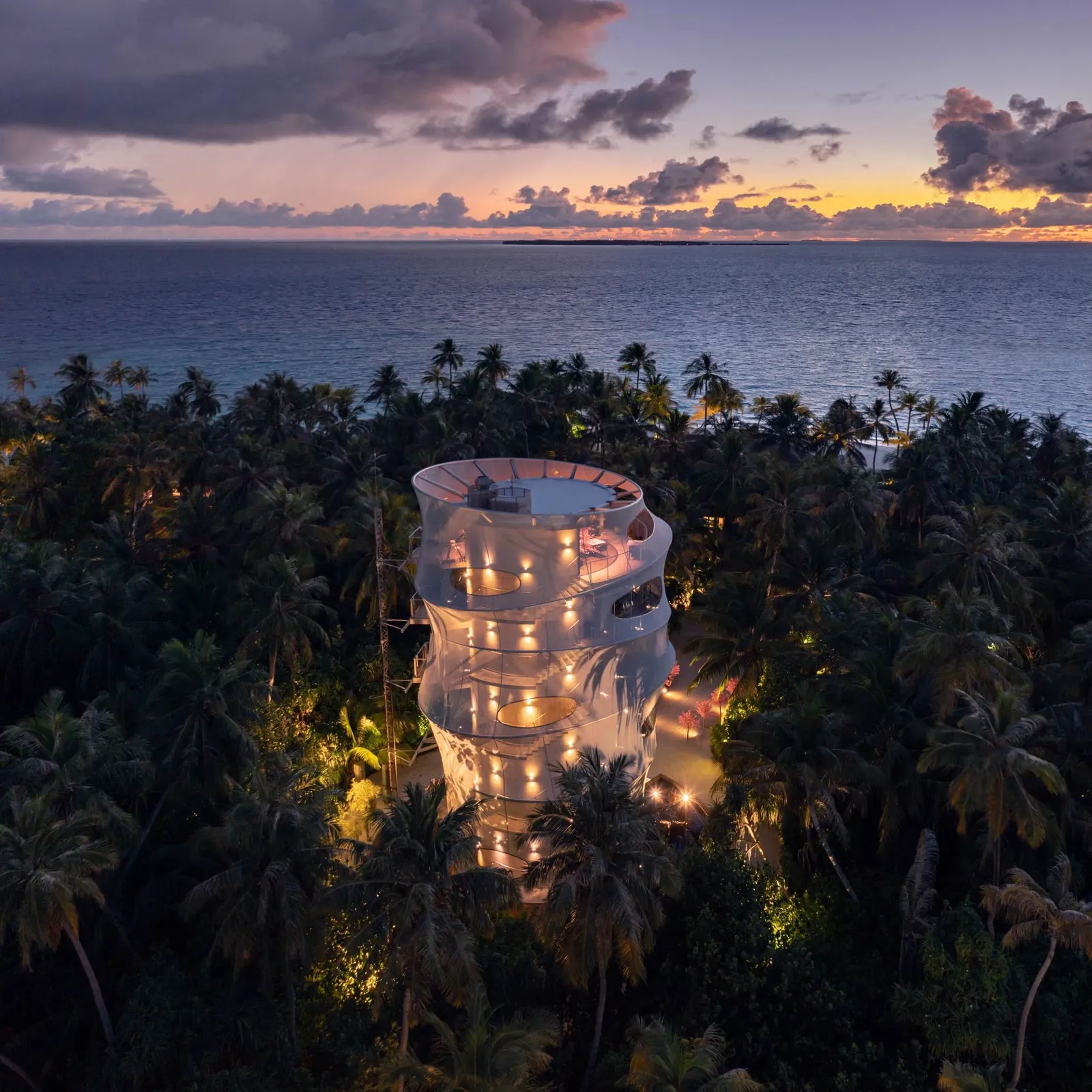 The Tavaru tower lit at night above the palm tops
