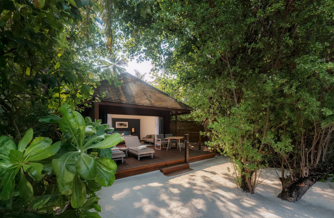 A Jacuzzi Beach Villa under the trees, its veranda on the sand.