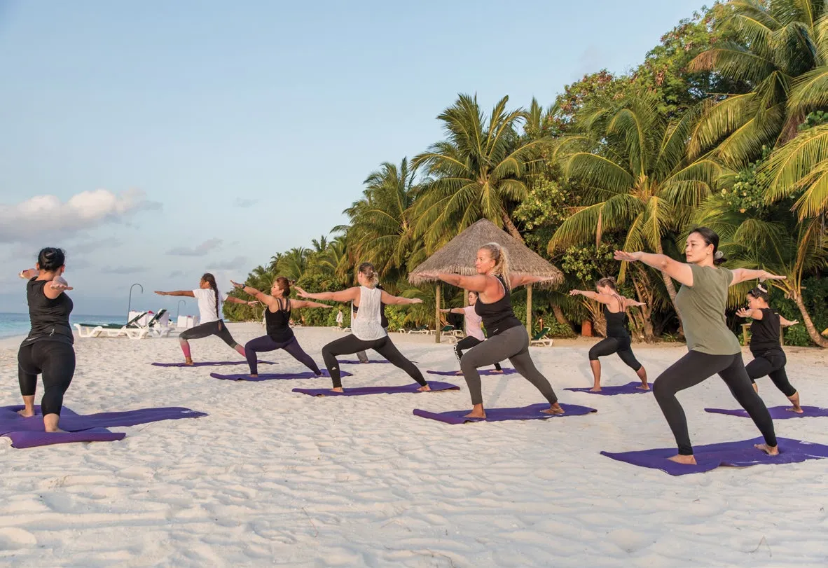 A yoga class on the beach, about 10 people on mats among the palms.