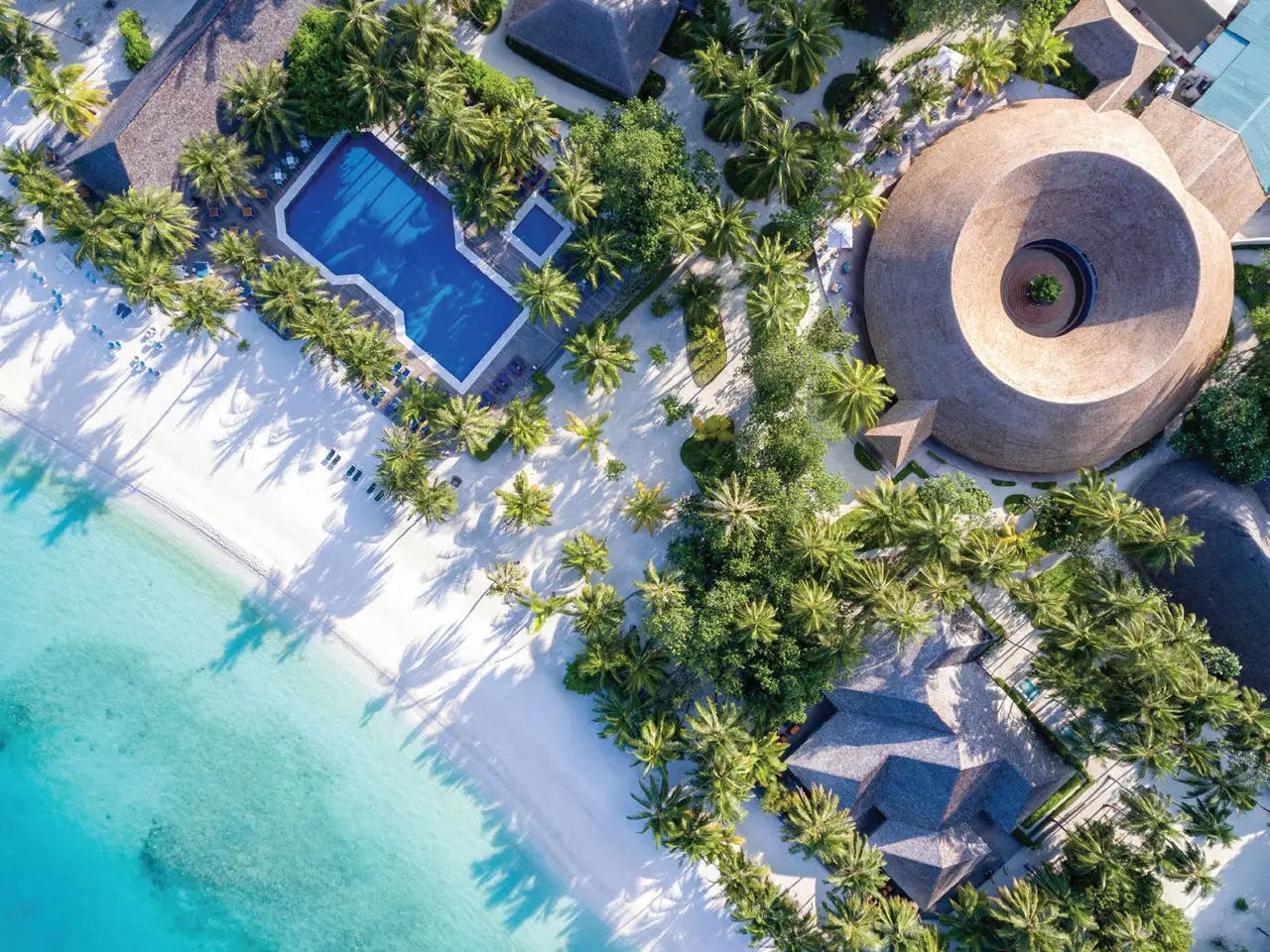 From above, a pool beside a round thatched building, a few steps from the beach.