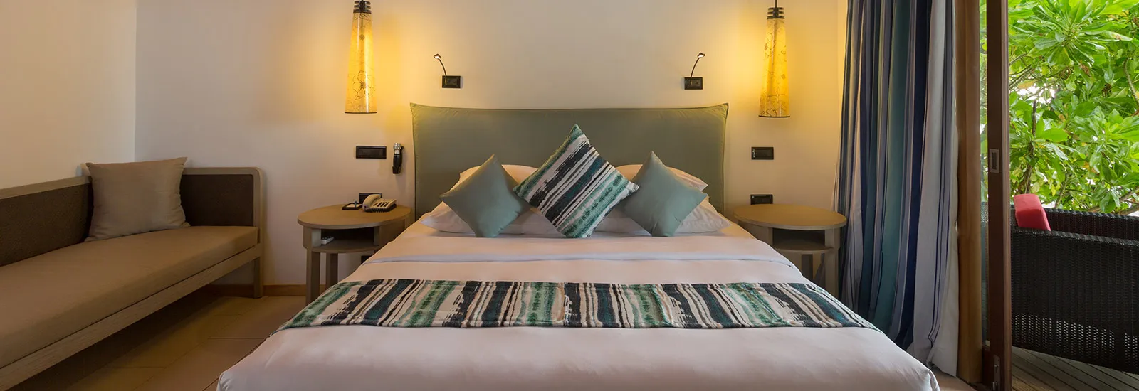 A Romantic Beachfront Villa: the king bed between 2 lamps, the sofa and the door open onto the porch among the green.