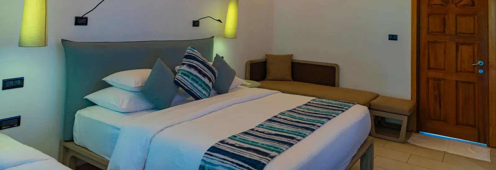 A Tropical Villa: the king bed with striped cushions, the sofa along the wall and the timber door.