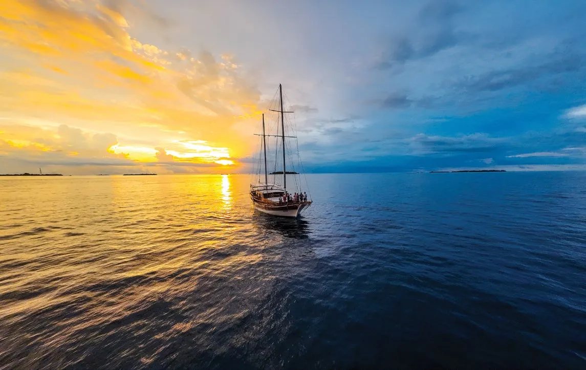 A 2-masted sailing boat on a calm sea at sunset.