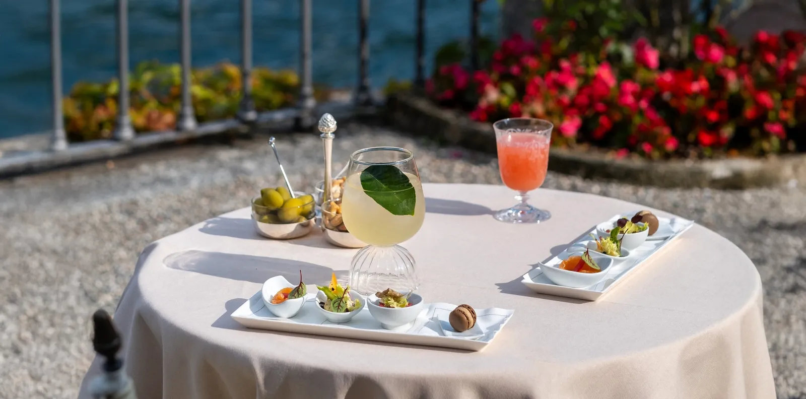 An aperitivo table on the Canova terrace, with red flowers and the lake