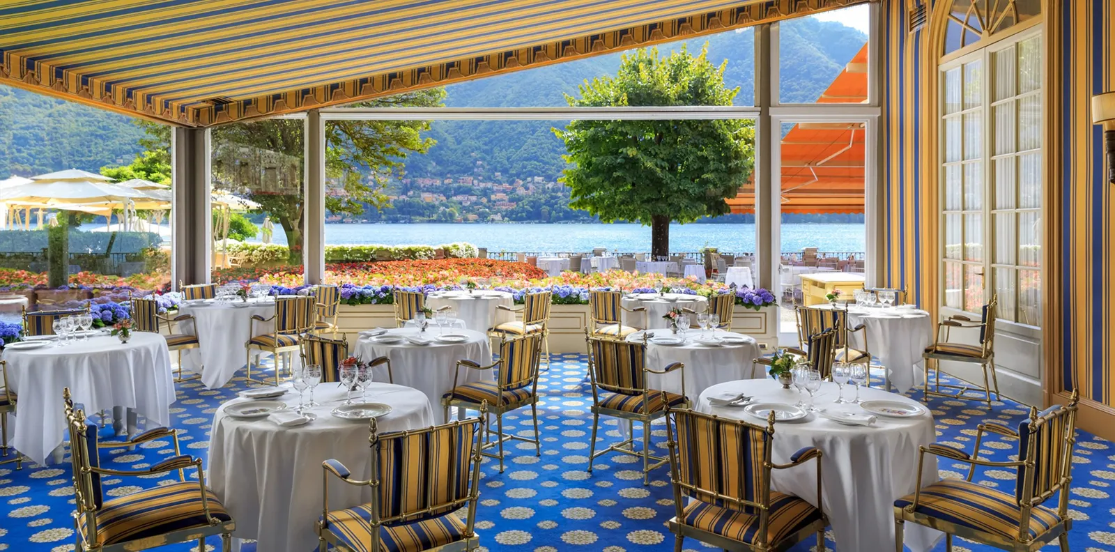 The Veranda dining room with laid tables and the lake beyond the glass walls