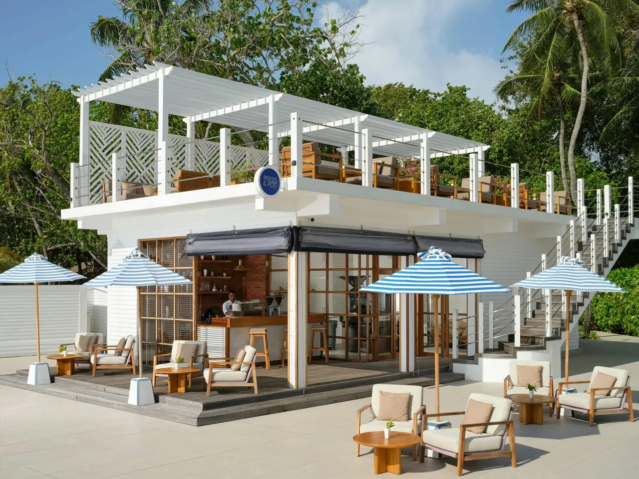 Press & Pot, the resort’s coffee house, with a terrace upstairs and striped parasols in front.