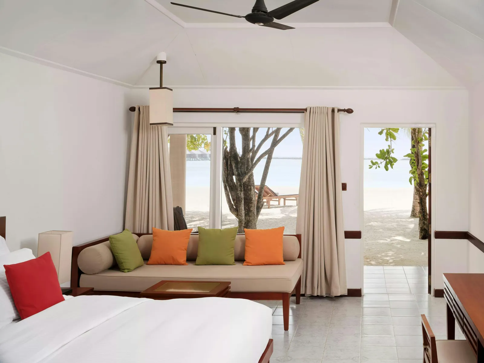 Inside a Beach Villa: the bed, a sofa with bright cushions and the door open to the beach.