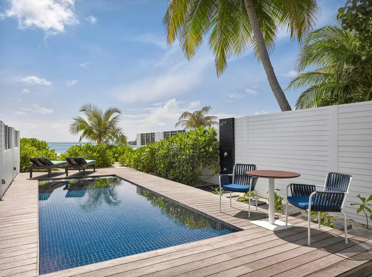 A Deluxe Beach Pool Villa’s private pool on its wooden deck, with a table and palms.