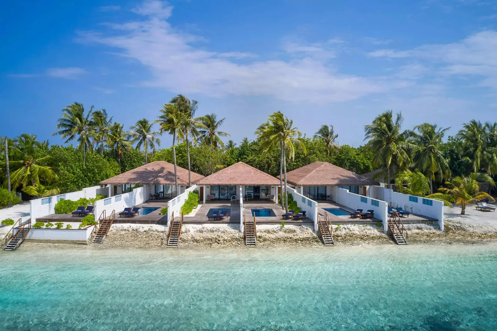 The Oceanfront Pool Villas from the sea: 3 houses with their pools on the sand and palms behind.