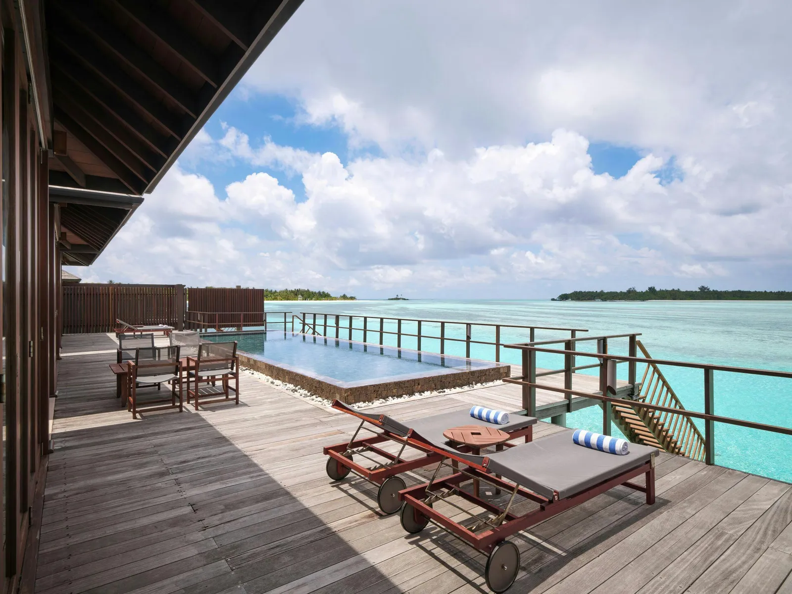 The deck of a 2-bedroom Ocean Suite with Pool, with loungers, the pool and the lagoon.