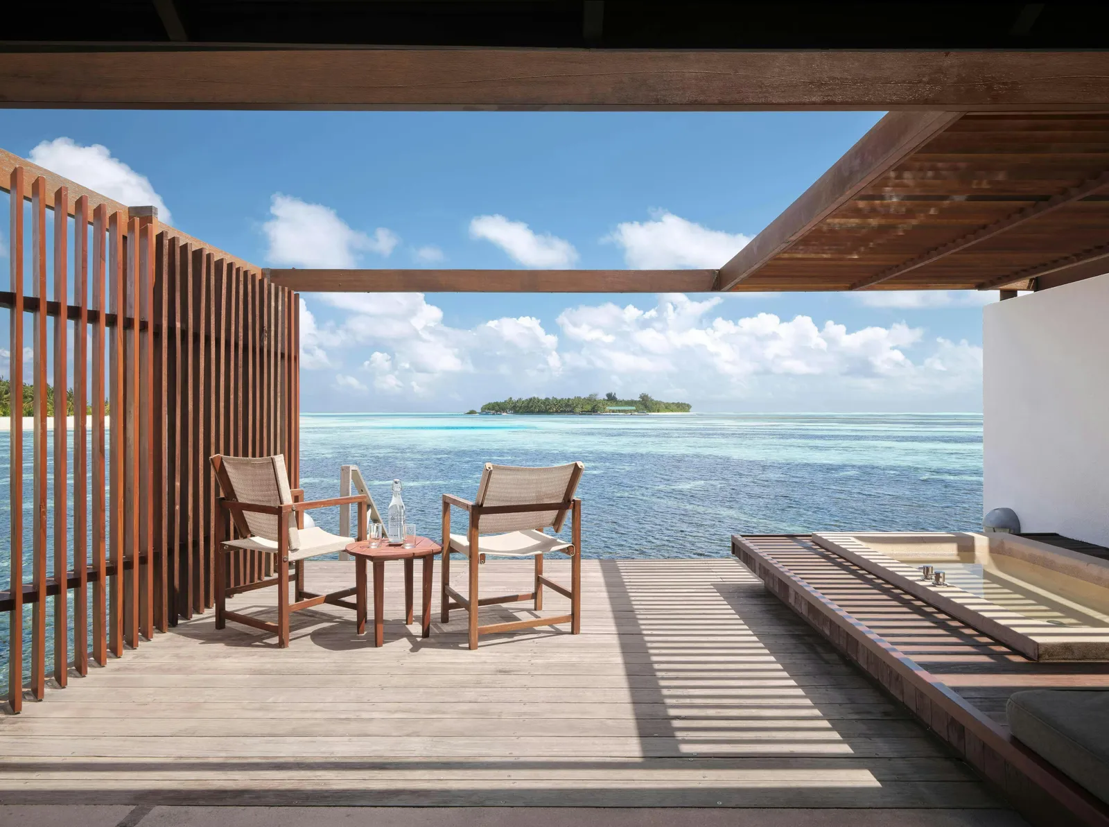 A Water Villa’s deck: 2 chairs, a timber screen and the lagoon with an island on the horizon.