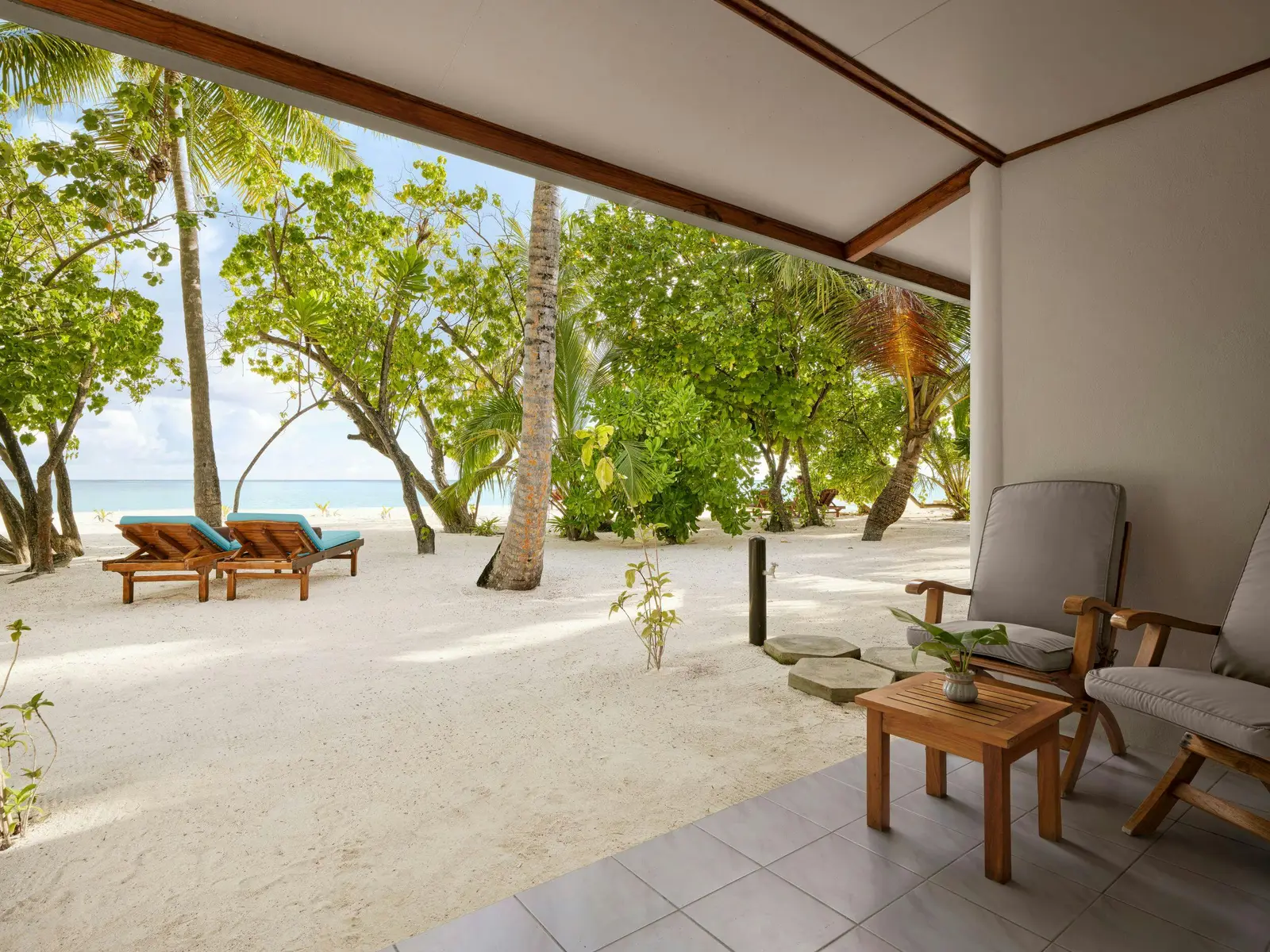 Veranda seating between trees and beach.