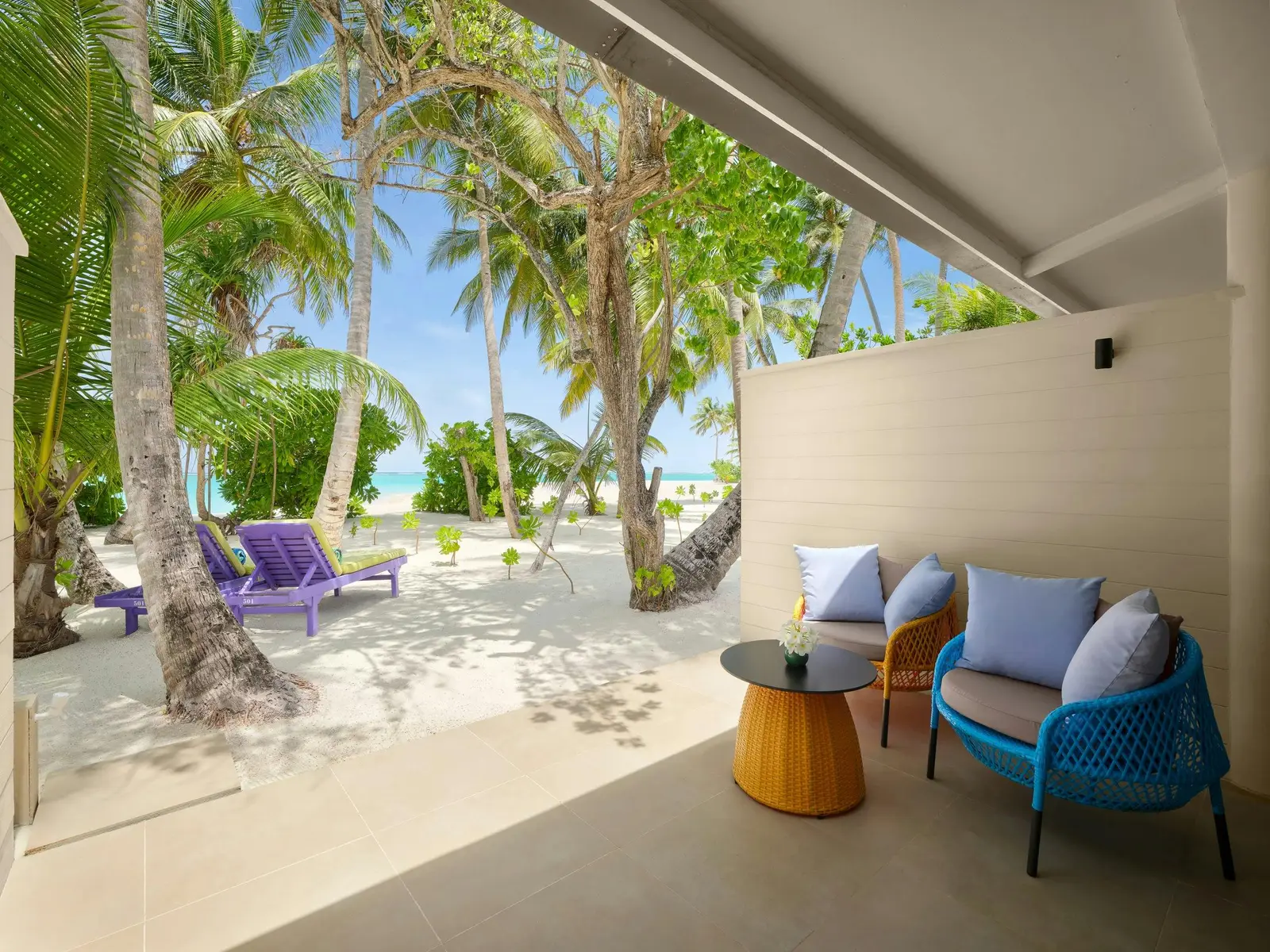 Sunset Deluxe Beach Villa — Covered beach-facing veranda with 2 chairs, side table and palms.