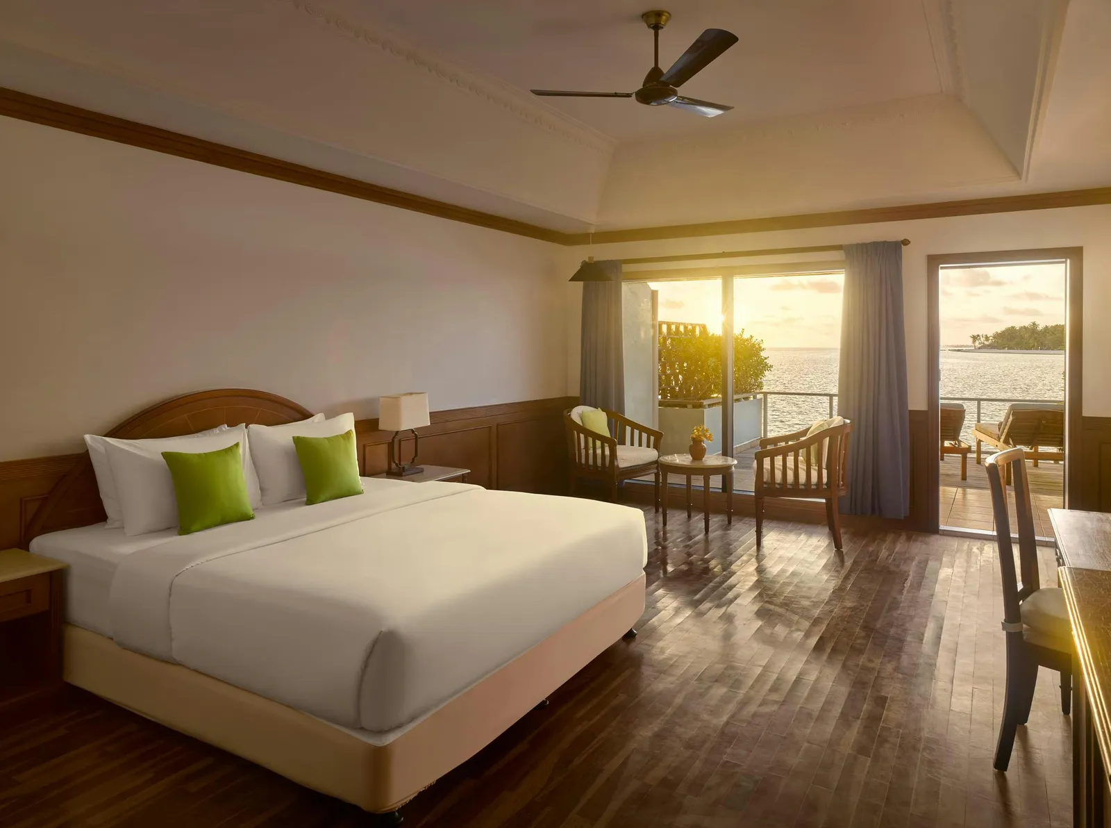Sunset Water Villa — Overwater bedroom at sunset with bed, desk and sea-facing terrace.