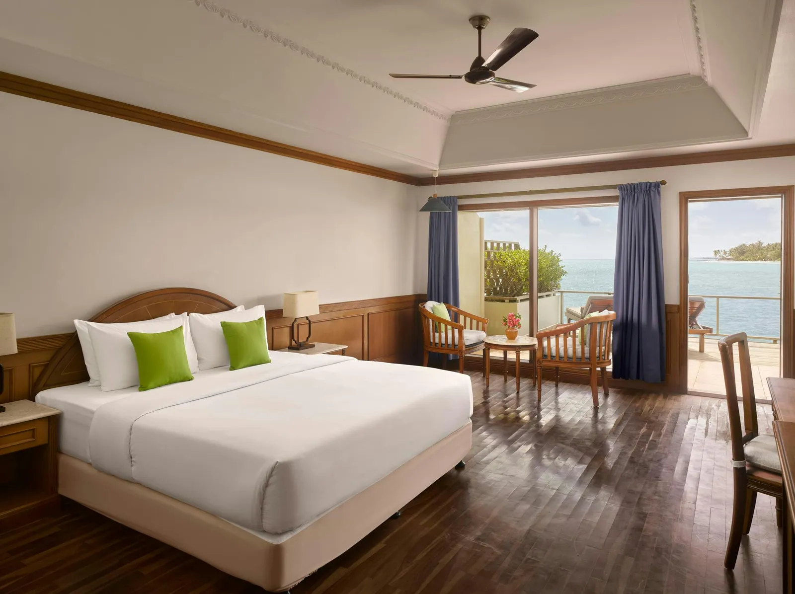 Water Villa — Overwater bedroom in daylight with bed, desk and sea-facing terrace.