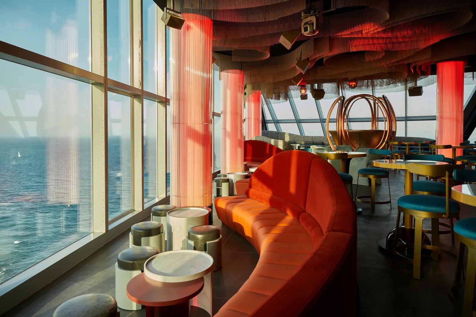 NOXE’s bar with an orange sofa, red columns and glass walls over the sea