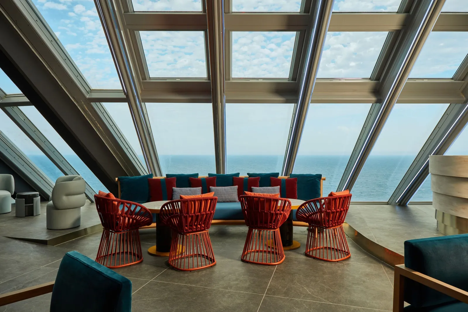 Red chairs at NOXE beneath the sloping glass roof, with the sea