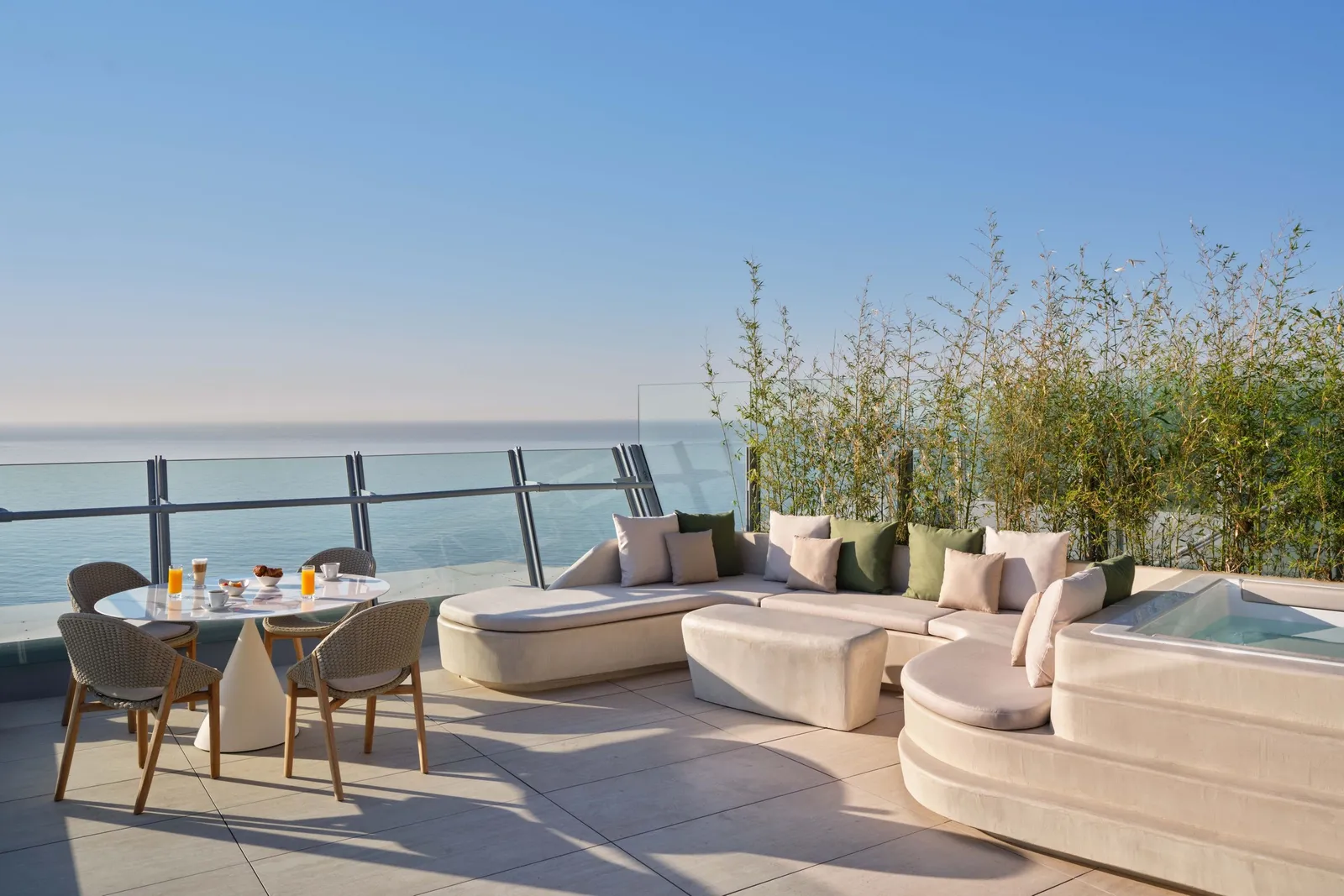 A white terrace with a curved sofa, a laid table and the sea beyond the balustrade